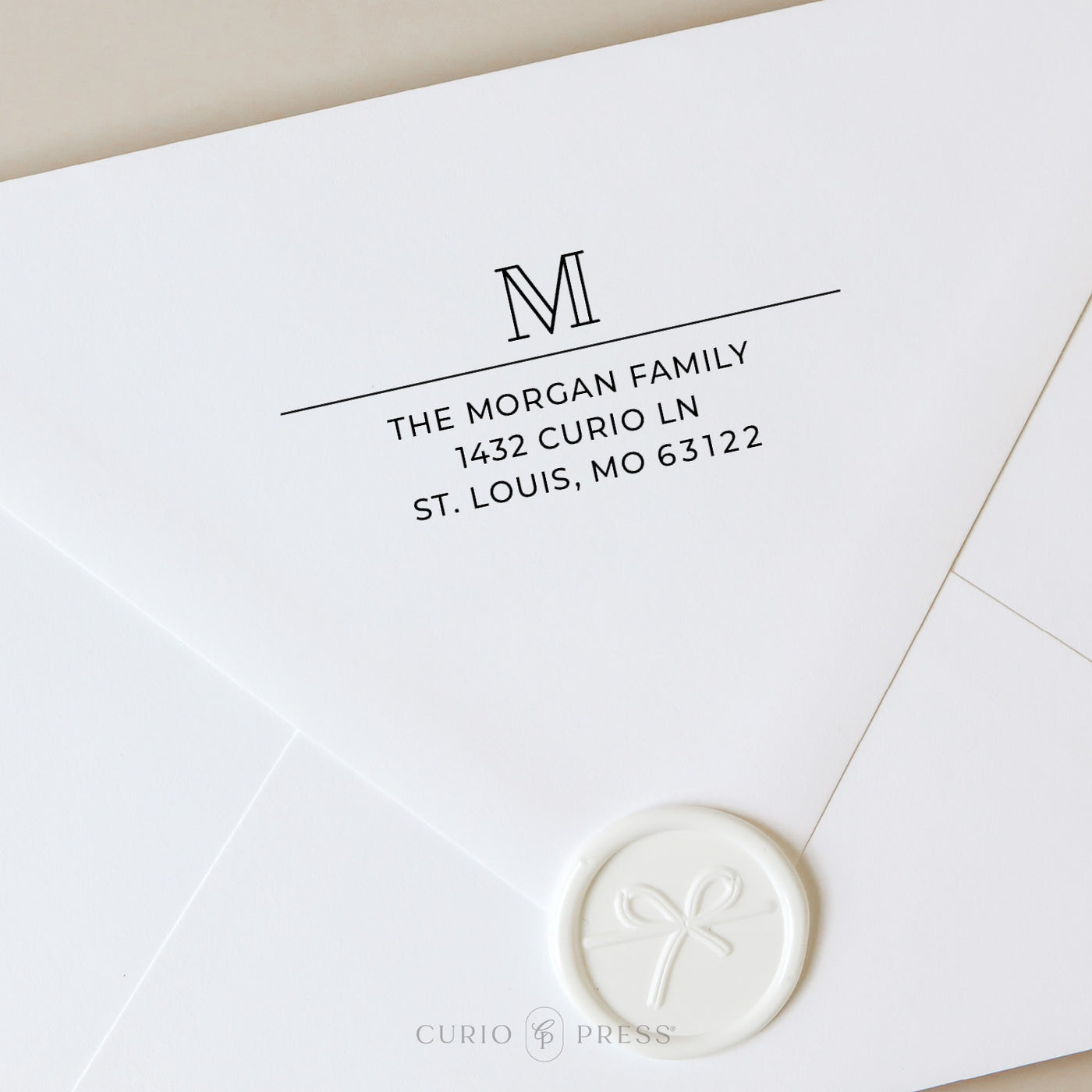 Return address stamp with bold outline monogram and clean printed name and address beneath a horizontal divider line