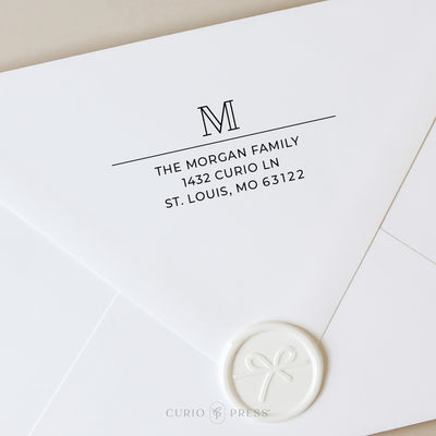 Return address stamp with bold outline monogram and clean printed name and address beneath a horizontal divider line