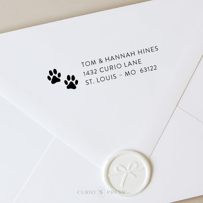 Custom address stamp with two paw prints and modern text, stamped in black ink on envelope, perfect for pet owners