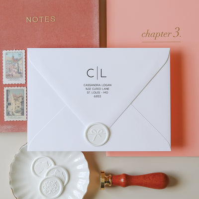 Modern monogram return address stamp on a white envelope styled with notebooks and wax seals