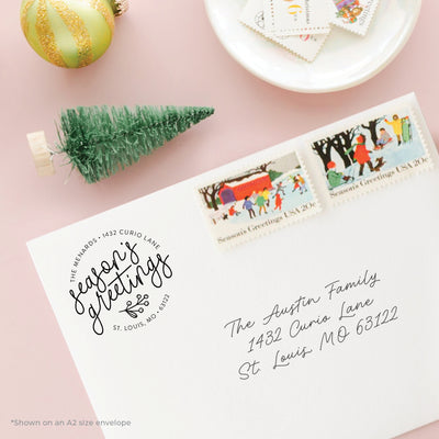 Custom Season's Greetings address stamp on an envelope with holiday stamps and pink background
