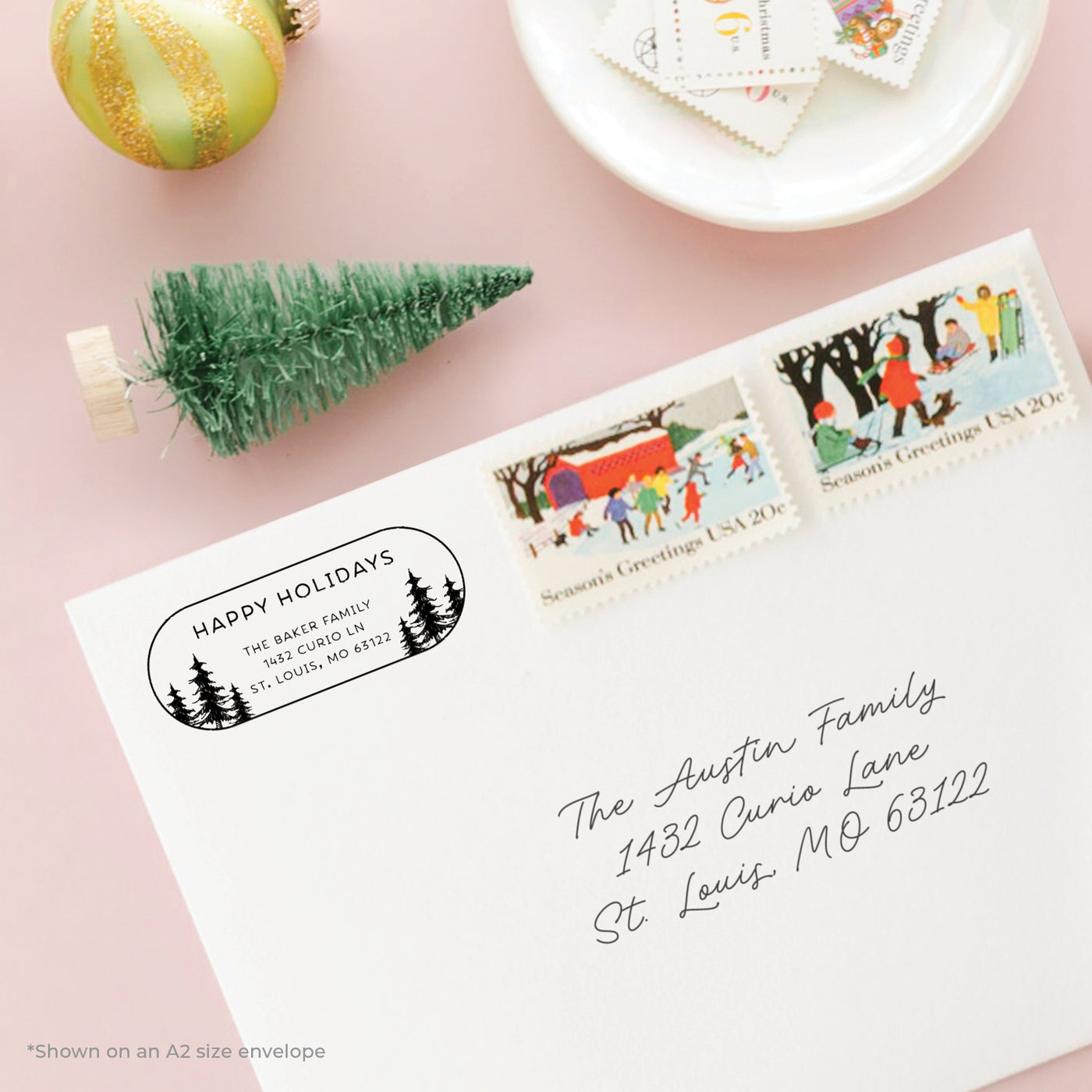 Holiday-themed personalized address stamp on envelope with seasonal stamps on a pink background