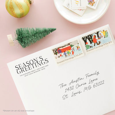 Holiday-themed personalized address stamp on envelope with Season's Greetings stamps on a pink background