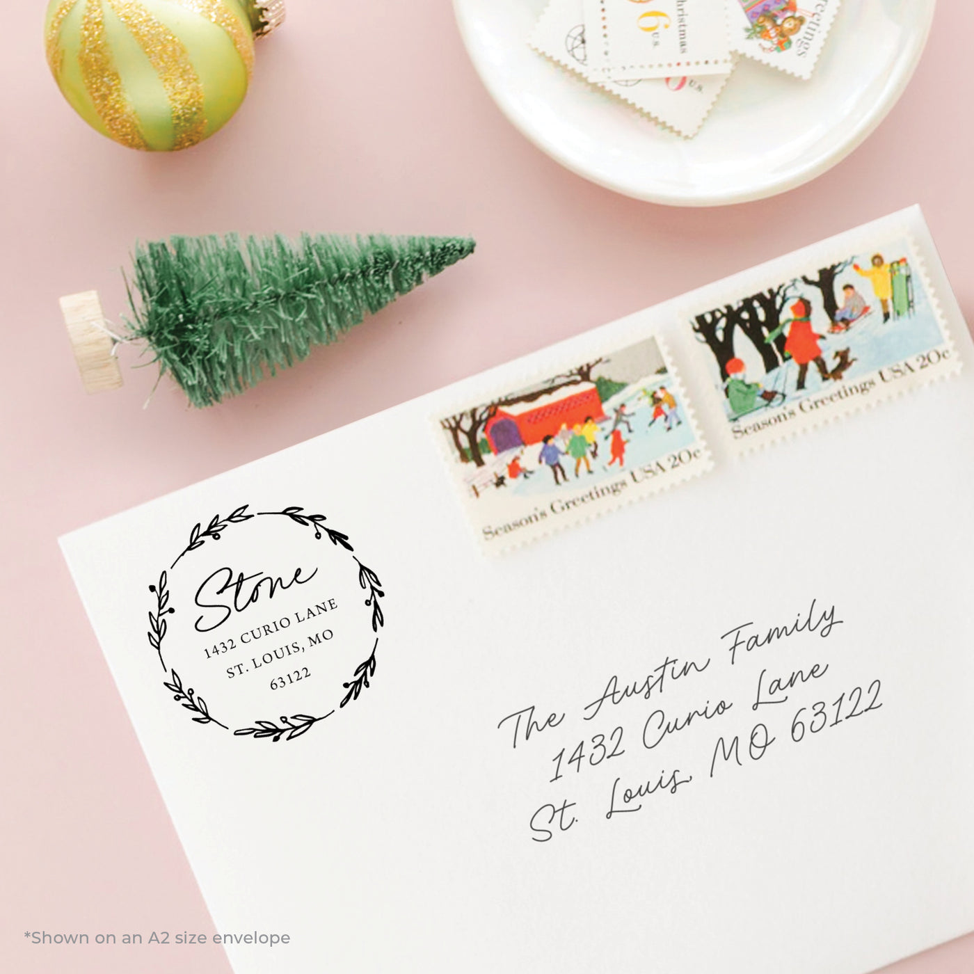 Holiday-themed personalized address stamp on envelope with Christmas stamps on a pink background